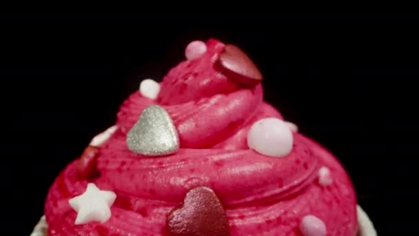 その上にピンクのフロスティングと銀のハートが付いている赤い包装のカップケーキ ドリースライダー クローズアップ — ストック動画