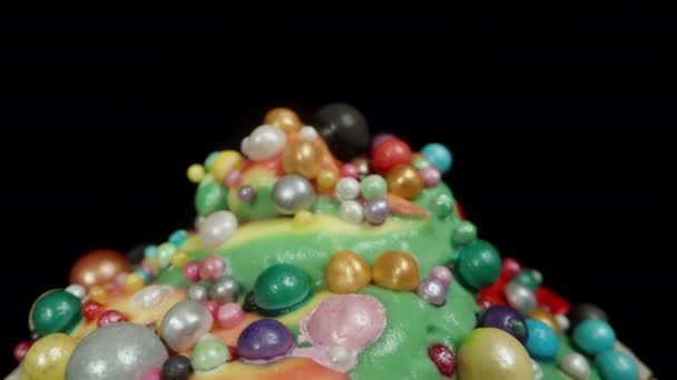 黒い背景に隔離された多色の虹のフロスティングとボールのカップケーキ ドリースライダー クローズアップ — ストック動画