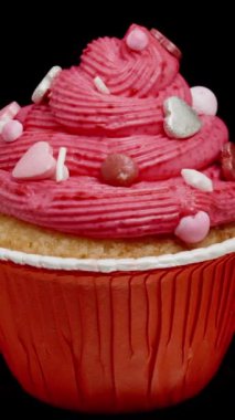 Pembe kremalı ve gümüş renkli şeker kalpli bir kek, siyah bir arka planda döngü halinde, izole edilmiş..
