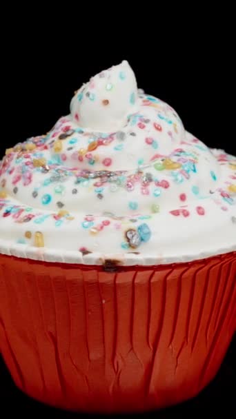 カラフルな砂糖で飾られた白いフロスティング付きのカップケーキ 隔離された黒い背景のループ回転 — ストック動画