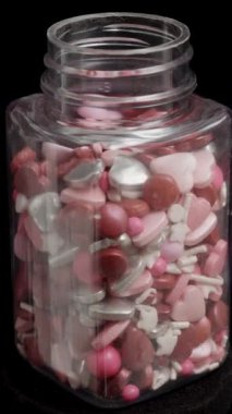 Kalp şeklinde bir kavanoz şeker süslemesi ve çok renkli toplar siyah arka planda bir döngü içinde dönüyor. İzole edilmiş.