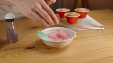 Şekerci kremaya kırmızı pudralı gıda boyası ekler. Kekler masada..