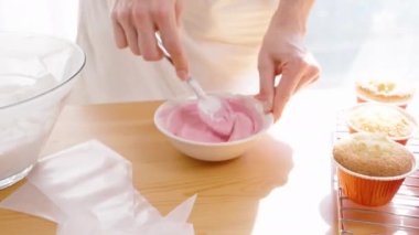 Pencereden gelen güneş ışığı, kadının kekleri süslemek için karıştırdığı pembe kremayı aydınlatıyor..