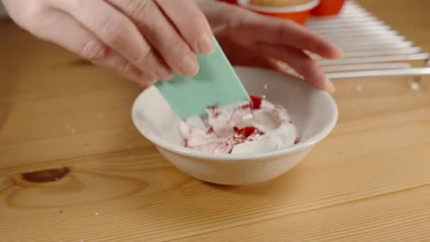 女性はそれを着色するために白いクリームに赤い食品着色の粉を混合しています — ストック動画