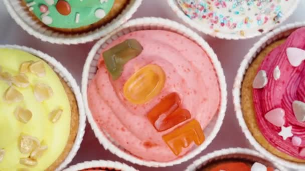 とさまざまなカラフルな砂糖の心を形成するゼリー文字で飾られたお祝いのカップケーキのトップビュー — ストック動画
