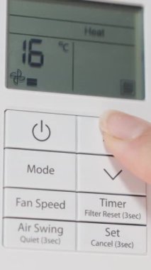 Dikey video. Beyaz bir duvardaki klima için uzaktan kumanda, bir kadın onu açar ve ısıtma modunda sıcaklığı maksimuma çıkarır..