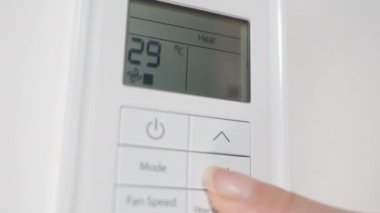 Duvardaki beyaz klimanın uzaktan kumandasını kapat, kadın sıcaklığı düşürür ve kapatır..