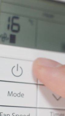 Dikey video. Yakından, adam beyaz uzaktan kumandalı klimayı açıyor ve sıcaklığı arttırıyor..