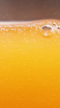 Dikey video. Portakal Suyu ya da Soda Macro Shot, Kabarcıklar ve Sıvı Seviyesi, Yavaş Hareket.