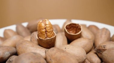 Çatlak ceviz kabuğu ikiye bölünmüş, fındık içeride, fındık yakın plan açık kahverengi arka planda dönüyor..