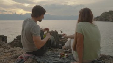 Erkek Kadın İçin Şampanya Döker, Gün batımı Deniz Kenarı Kayalıkları Üzerine Tarih. Battaniyede Çilek.