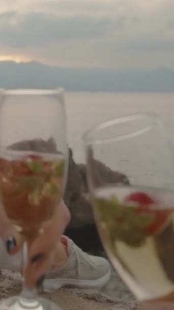 垂直录像 第一人称观 与女人一起倒入一杯香槟 坐在海边的毛毯上 欣赏日落 玻璃杯中的草莓 — 图库视频影像