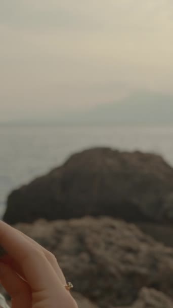 垂直录像 日落时 长头发的女人坐在海边的岩石上吃草莓 — 图库视频影像