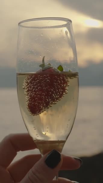 垂直录像 镜头从一杯香槟和草莓转移到遥远的大海中的群山和云中的太阳 — 图库视频影像