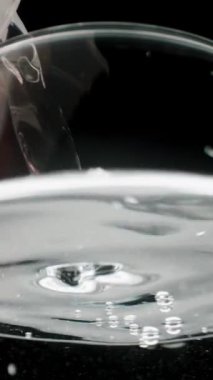 Dikey video. Düşük açılı bir su bardağının görüntüsü, ölçüm kabından akan suyun gümüş yüzeyi. Yavaş çekim makrosu.