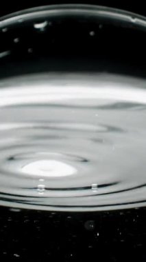 Dikey video. Cama damlayan su damlacıkları, cıvayı andıran suyun gümüşi yüzeyinin düşük açılı makro görüntüsü..