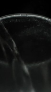 Dikey video. Sıcak su bir çaydanlıktan bir bardağa dökülüyor, buhar ve su kabarcıkları ile. Suyun gümüşi yüzeyinin altından bak.