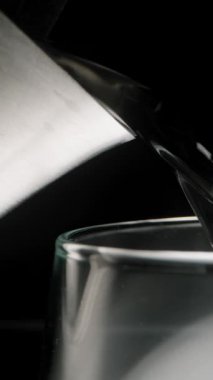 Dikey video. Metal bir çaydanlıktan bardağa kaynar su dökülüyor. Siyah bir arkaplanda, yakın plan.