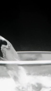 Dikey video. Cam ağzına kadar kaynar suyla doluyor ve buhar yavaşça siyah zemine doğru yükseliyor. Yakın plan..