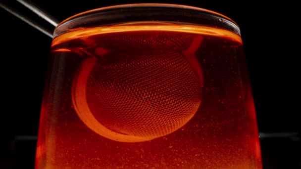 水に浸された葉で金属ふるいを使用してガラスで黒茶を準備する — ストック動画