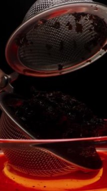 Dikey video. Bir el, içinde kuru yapraklar olan çay demleme cihazını açar. Metal bir ağ küresi.