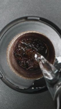 Dikey video. Kamera gittikçe alçalıyor ve Sieve 'in içinde demlenen çay için kaynar su dökülüyor. Makro Kaydırıcı.