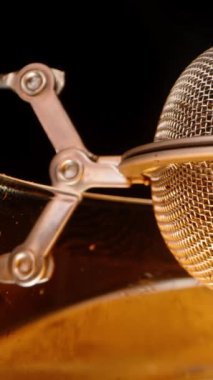 Dikey video. İçindeki çay yapraklarının bardakta demlenmek için olduğu ağdan metalik bir küre. Siyah arkaplanda makro.