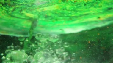 Yeşil bir yüzeydeki su altı görüntüsü, içine sıvı dökülüyor ve su altında kabarcıklar yayılıyor..