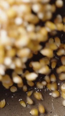 Dikey video. Patlamış mısır için mısır taneleri tavadaki kızgın yağın içine dökülüyor, yavaş çekimde üst görüntü.