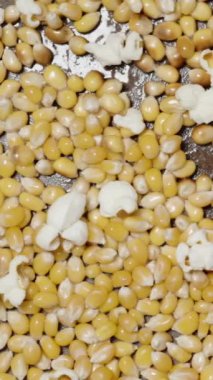 Dikey video. Mısır taneleri yağda kızarır ve tavada patlar, üst görüntü yavaş çekimde..