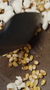 Dikey video. Tavada patlamış mısır karıştırılır ve patlar. Yavaş çekim üst görünümü.