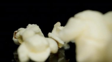 Patlamış mısır siyah aynalı arka plana düşer, kamera geriye doğru hareket eder. Makro bebek. Yavaş çekim.