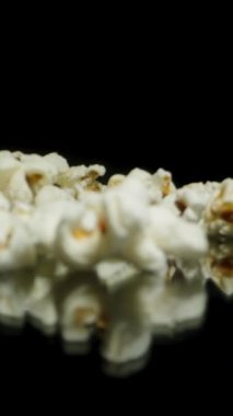 Dikey video. Elden bir avuç patlamış mısır siyah arka plana dökülüyor. Makro yavaş çekim.