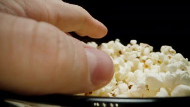 Büyük cam bir kase patlamış mısır. Bir el yavaşça yaklaşıyor ve bir avuç alıyor. Dolly 'yi yakın çekim. Siyah bir arkaplanda izole edilmiş.