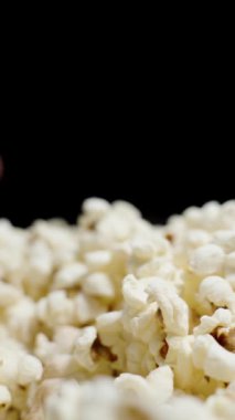 Dikey video. Eller her iki taraftan da karanlıktan belirir ve bir avuç patlamış mısır alır. Yakın çekim, yavaş çekim.