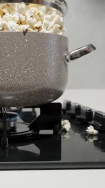 Dikey video. Tencerenin kapağı, içerideki patlamış mısırın gaz sobasının kenarından dökülmesi yüzünden yükseliyor..