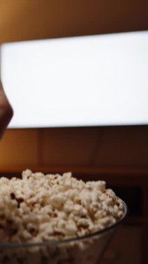 Dikey video. Kamera, kadın televizyonun önünde patlamış mısır yerken boş beyaz bir ekranın maketini izliyor..