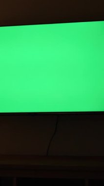 Dikey video. Karanlık bir odada, elinde lamba ve bir kase patlamış mısırla uzanan yeşil ekran bir televizyonun maketi..