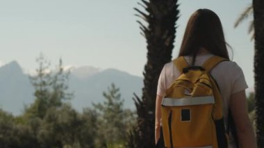 Sırt çantalı bir kadın turist güneş ışığı altında parkta geziniyor. Uzakta dağlar, görünen karlı zirveler..