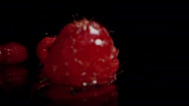 Kırmızı ahududu üzümleri ıslak, siyah bir yüzeye düşüyor ve etrafa su sıçrıyor. Ağır çekim. Dolly kaydırıcı, kapat..