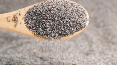 Arka planda haşhaş tohumları ve ön plandaki tahta kaşıktan dökülen bir avuç haşhaş tohumu..