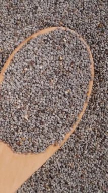 Dikey video. Ahşap kaşıktan düşen haşhaş tohumlarının yakın çekim döndürülmüş videosu..