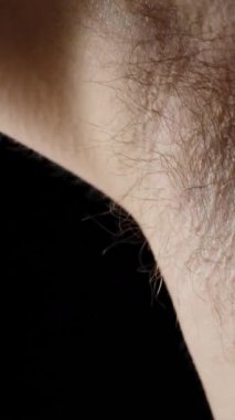 Dikey video. Bir adam elini kaldırır ve kıllı koltuk altının altına cömertçe deodorant sıkar. Yakın plan. Yavaş çekim.
