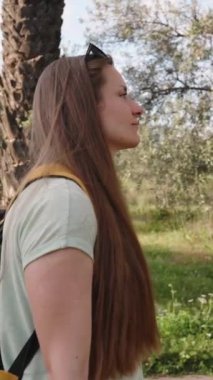 Dikey video. Kamera, sırt çantasıyla yolda yürüyen genç bir kadının etrafında dönüyor. Palmiye manzarasına bayılıyor..