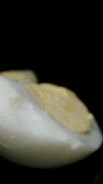 Dikey video. Kaynamış yumurtalardan oluşan yarımlar masanın üzerine, kamera aralarından süzülürken siyah bir arka plana doğru saçılırlar. Dolly kaydırıcı, yakın plan..