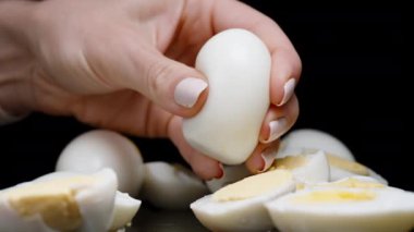 Bir kadının eli haşlanmış bir yumurtayı sıkar ve her yöne doğru uçan küçük parçalara ayırır. Ağır çekim. Siyah bir arkaplana karşı.