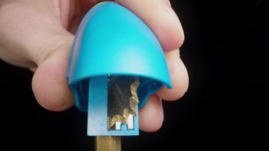 Bir adam siyah arka planda mavi bir bileyicide bir kalemi keskinleştirir. Yakın plan..