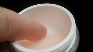 Bir adamın parmağı kavanozdaki nemlendirici pembe kreme batıyor. Yakın plan..