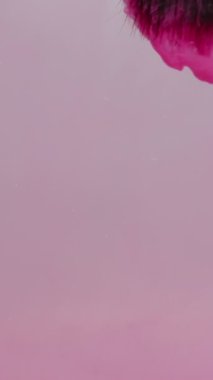 Dikey video. Ressam pembe suluboya boyasının fırçasını temizliyor ve suda soyut renkli bir sıçrama yaratıyor. Mürekkep suyun altında dönüyor..