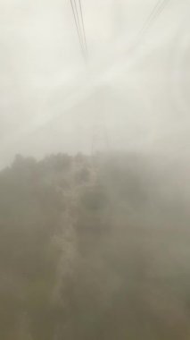 Yoğun bulutların arasında bir teleferiğe binmek. Dağa çıkan uzun metal direkler..